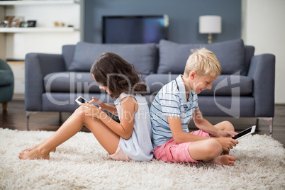 Siblings using digital tablet and mobile phone in living room
