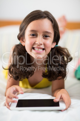 Portrait of smiling girl with digital tablet lying on bed