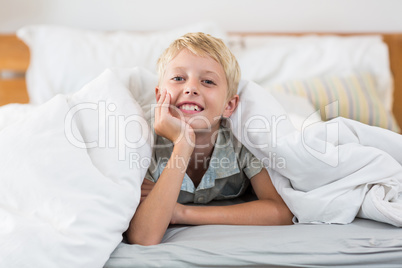 Portrait of smiling boy lying under bed sheet in bedroom