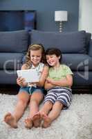 Siblings using digital tablet in living room