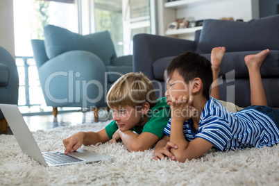 Siblings lying on rug and using laptop in living room