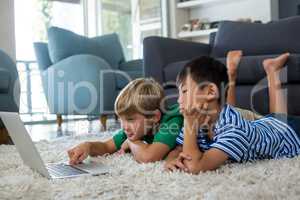 Siblings lying on rug and using laptop in living room