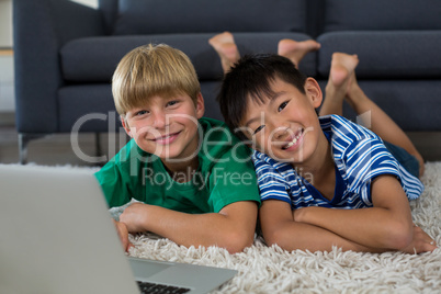 Portrait of smiling siblings with laptop lying on rug