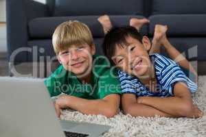 Portrait of smiling siblings with laptop lying on rug