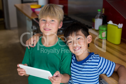 Portrait of smiling siblings using digital tablet in kitchen