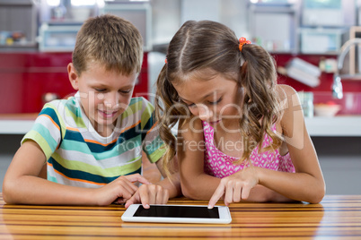 Smiling siblings using digital tablet in kitchen