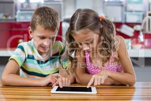 Smiling siblings using digital tablet in kitchen