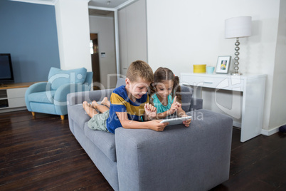 Siblings using digital tablet in living room