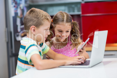 Siblings using laptop and mobile phone in kitchen