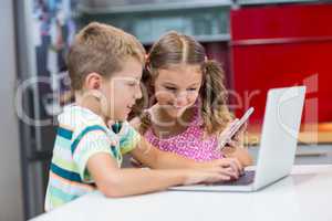 Siblings using laptop and mobile phone in kitchen