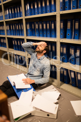 Frustrated businessman with file and papers sitting in storage room