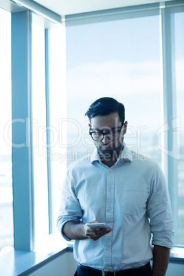Young businessman using mobile phone while standing against glass window
