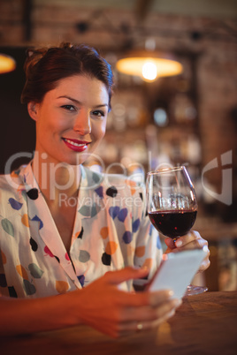 Portrait of young woman using mobile phone while having wine