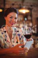 Portrait of young woman using mobile phone while having wine