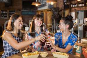 Happy female friends holding toasting beer bottles