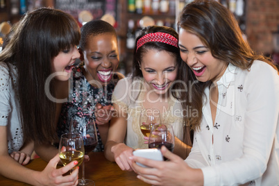 Happy female friends with wineglasses using mobile phone