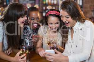Happy female friends with wineglasses using mobile phone