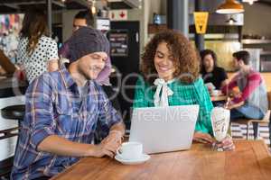 Smiling friends using laptop in restaurant