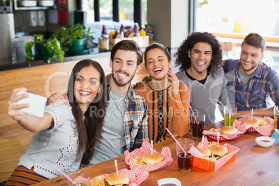 Woman taking selfie with cheerful friends in restaurant