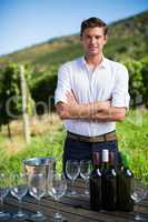 Portrait of man standing by wineglasses and bottles on table