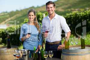 Portrait of friends holding wineglasses by table against vineyard