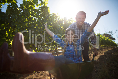 Portrait of happy man pushing his cheerful girlfriend in wheelbarrow at vineyard
