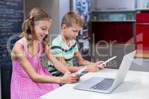 Siblings using digital tablet and mobile phone in kitchen