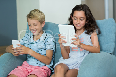 Siblings using digital tablet and mobile phone in living room
