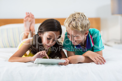 Smiling siblings using digital tablet on bed in bedroom