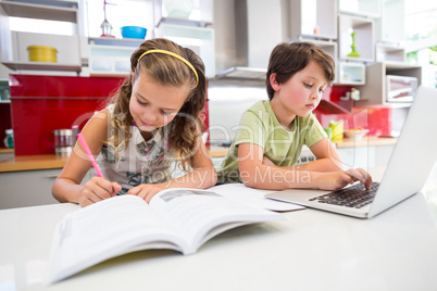 Girl doing her homework while boy using laptop in kitchen