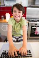 Portrait of smiling boy using laptop in kitchen