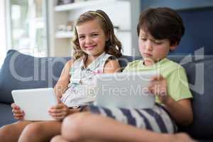 Siblings using digital tablet in living room