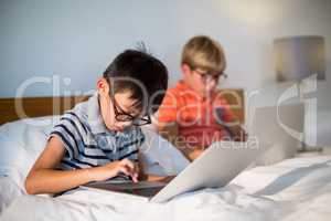 Smiling siblings using laptop on bed