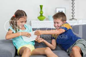 Siblings fighting over digital tablet in living room
