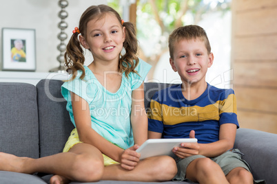 Portrait of siblings with digital tablet sitting on sofa in living room