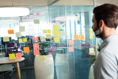 Businessman looking at adhesive notes and strategy on glass