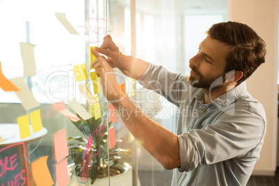 Young businessman sticking adhesive notes on glass