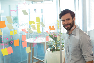 Portrait of smiling businessman standing by adhesive notes on glass