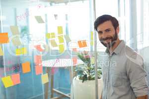 Portrait of smiling businessman standing by adhesive notes on glass