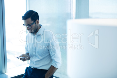 Young businessman using mobile phone while leaning on glass window