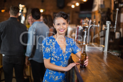 Portrait of smiling woman holding beer bottle in pub