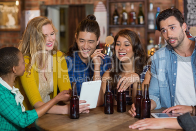 Happy friends with beer bottles using digital tablet