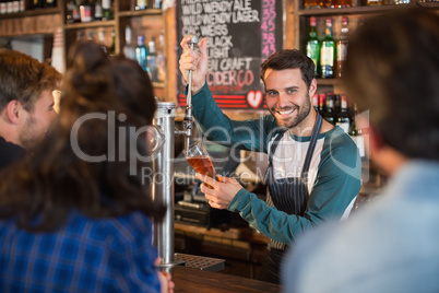 Smiling bartender pouring beer in glass for customers