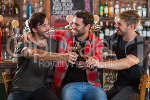 Happy young male friends toasting beer bottles in bar