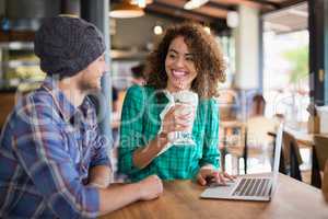 Smiling woman having smoothie while looking at male friend sitting together