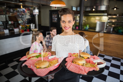 Waitress serving burger while customers sitting in restaurant