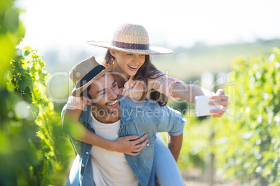 Happy couple taking selfie while piggybacking at vineyard