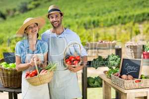 Portrait of smiling couple holding fresh vegetables in baskets