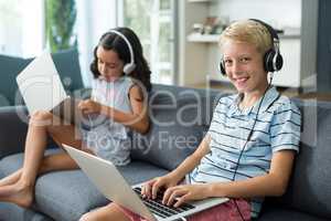 Siblings listening to music while using laptop in living room