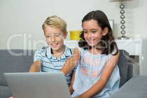 Smiling siblings using laptop in living room